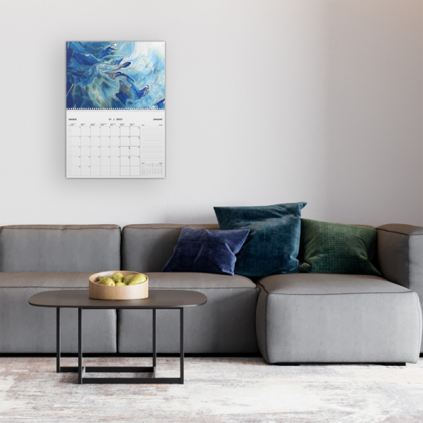 Sofa su trim pagalvėm, staliukas ir kalendorius ant sienos.